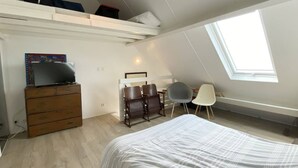 Un dormitorio con cama, cómoda, televisión, escritorio con dos sillas y tragaluz.