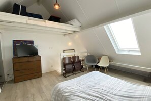 A bedroom with a bed, a dresser, a TV, a desk with two chairs, and a skylight.