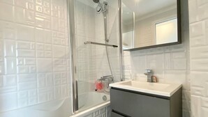 Un baño con cabina de ducha de vidrio, un lavamanos blanco y un espejo sobre él.