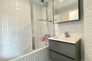 A bathroom with a glass shower enclosure, a white sink, and a mirror above it.