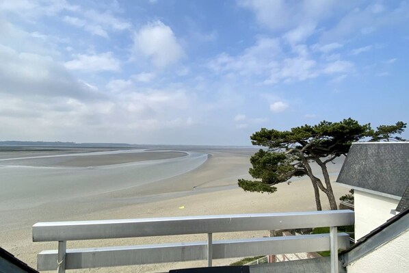 A coastal view with a sandy beach, a tree, and a building with a sloped roof. - Appartement Avec Terrasse , Surplombant la Baie de Somme (Le Crotoy)