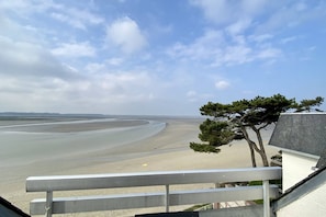 A coastal view with a sandy beach, a tree, and a building with a sloped roof. - Appartement Avec Terrasse , Surplombant la Baie de Somme (Le Crotoy)