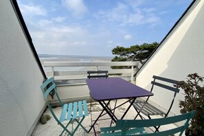 A balcony with a table and chairs, overlooking a beach.