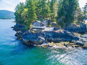 A house on a rocky shoreline with a dock extending into the water, surrounded by dense forest.