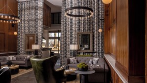 Un salon moderne avec un canapé gris, un fauteuil vert et une table basse. On y trouve des rideaux à motifs et un lustre.