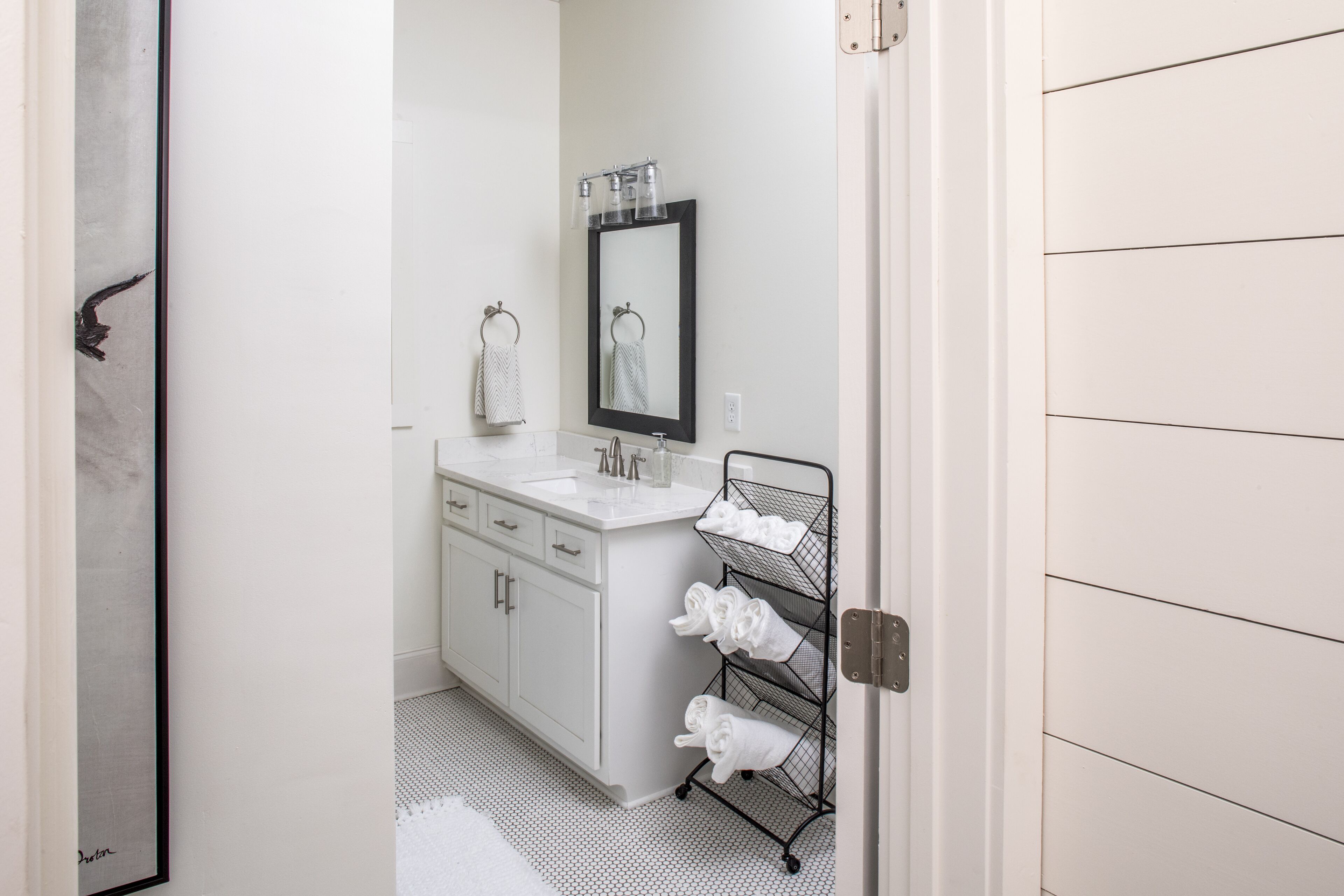 Un baño con lavamanos blanco, espejo y toallero.