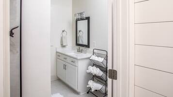 Un baño con lavamanos blanco, espejo y toallero.