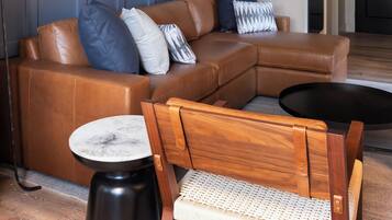 Una sala moderna con un sofá seccional de cuero marrón, una mesa de centro redonda de madera y una pequeña mesa redonda con cubierta de mármol.