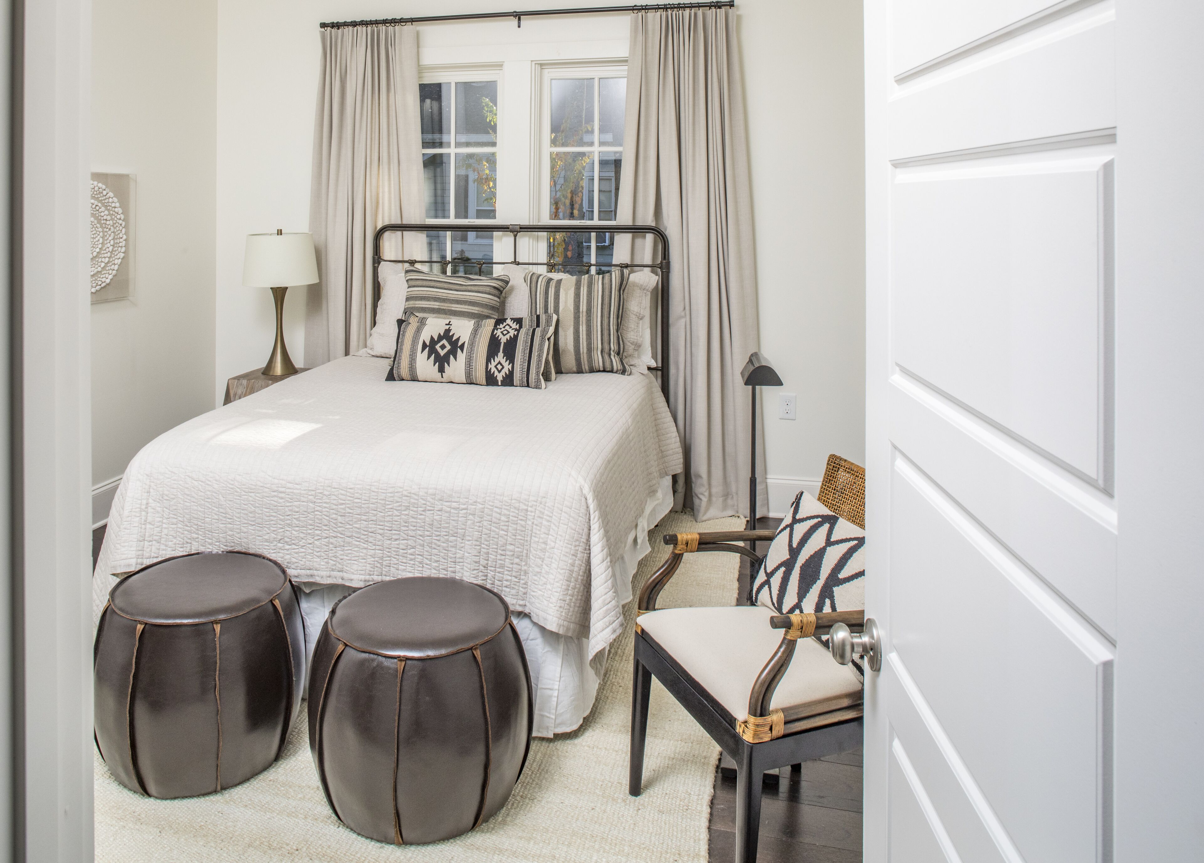 Une chambre à coucher bien rangée, avec un lit, des lampes de chevet, une chaise et deux poufs.