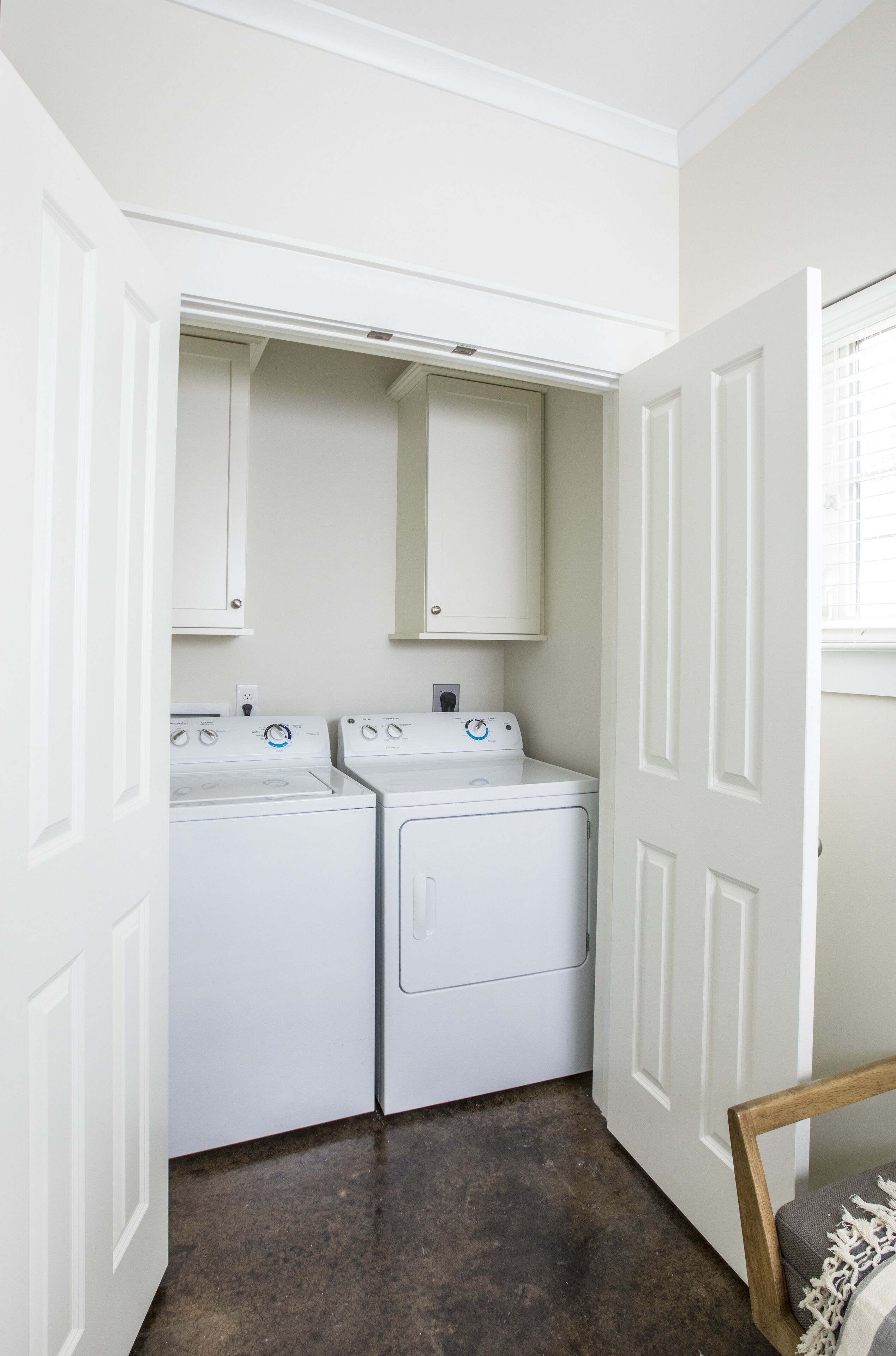 A laundry room with two white front-loading washers and dryers, white cabinets above, and a wooden door frame.