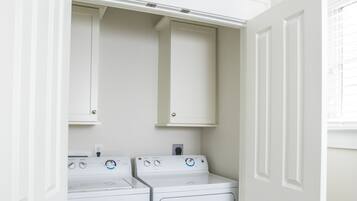 A laundry room with two white front-loading washers and dryers, white cabinets above, and a wooden door frame.