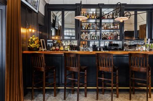 Uma área de bar com cadeiras de madeira, balcão e prateleiras cheias de garrafas.