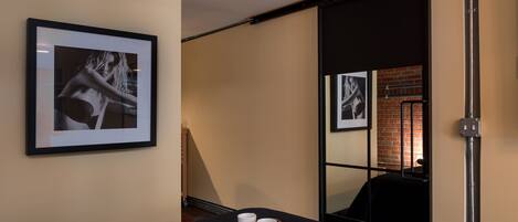 A hotel room with a bed, a tray with two cups and a bar of soap, a framed picture on the wall, and a sliding door leading to a brick wall.
