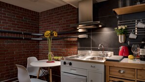 A kitchen with a brick wall, a white countertop, a sink, and a stove. There are white chairs and a table with a vase of flowers. - Queen Anne Design Studio, 7days max. (Seattle)