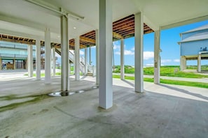 Un espace extérieur ouvert et abrité, doté d’un sol en béton et de piliers blancs, qui mène à un bâtiment à la façade bleue.