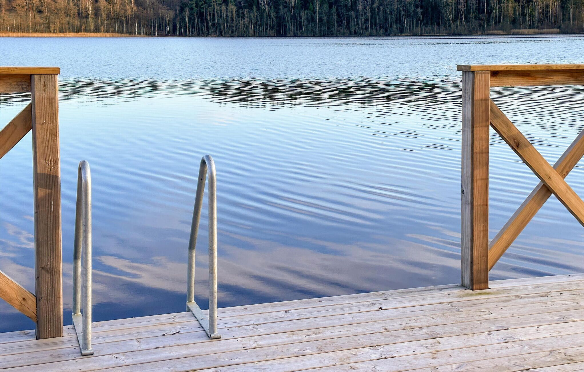 Un muelle de madera que se extiende sobre aguas tranquilas, con un bosque al fondo.