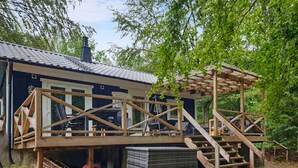 A wooden deck with a pergola, a staircase, and a small building with a dark roof.