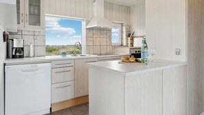 Ett modernt kök med vita skåp, ett stort fönster och utsikt över omgivningarna.