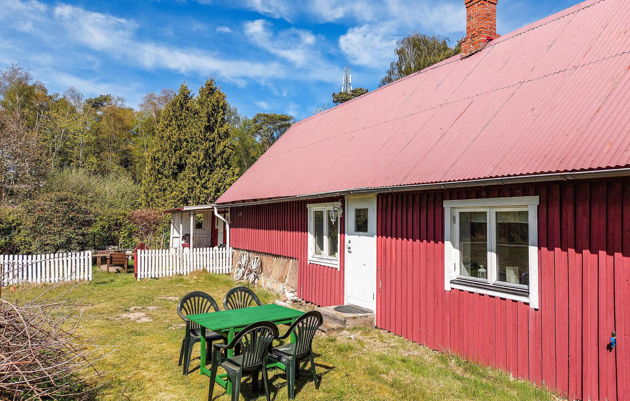 Een rode houten woning met een witte deur, een veranda en een groene tafel met stoelen.