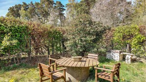 An outdoor wooden table and chairs set in a garden with a stone wall and dense foliage in the background. - Awesome home in Eldsberga with kitchen (Eldsberga)