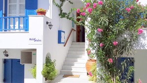 Ein weißes Gebäude mit blauen Fensterläden, einer Treppe und einem Blumentopf mit rosa Blüten.