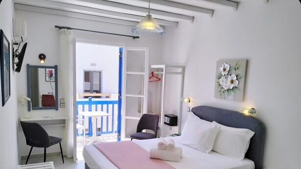 Ein Hotelzimmer mit Bett, Schreibtisch, Stuhl, Kleiderschrank und einem Balkon mit blauer Brüstung.