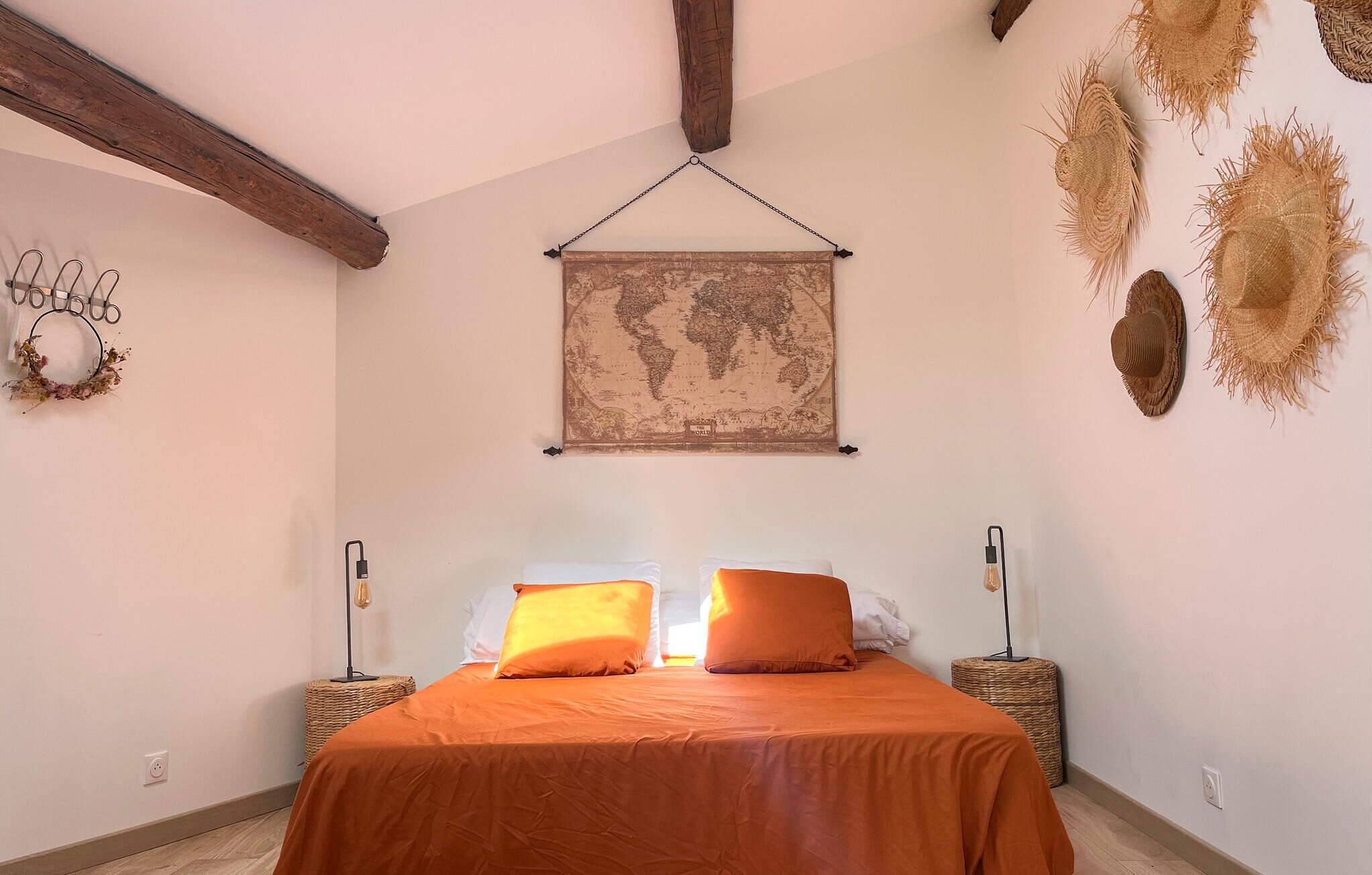 A bedroom with a bed, two bedside tables, a hanging world map, and decorative wall hangings.