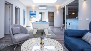A modern living room with a pool table, a blue sofa, and a round coffee table with a bottle and glass. - Stunning 4 Bedroom Villa on Prestigious Development (Playa Blanca)