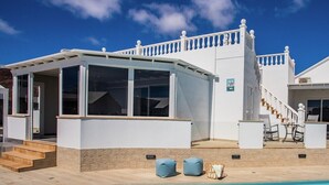 A modern poolside area with a clear blue pool, white building with a balcony, and outdoor seating. - Stunning 4 Bedroom Villa on Prestigious Development (Playa Blanca)