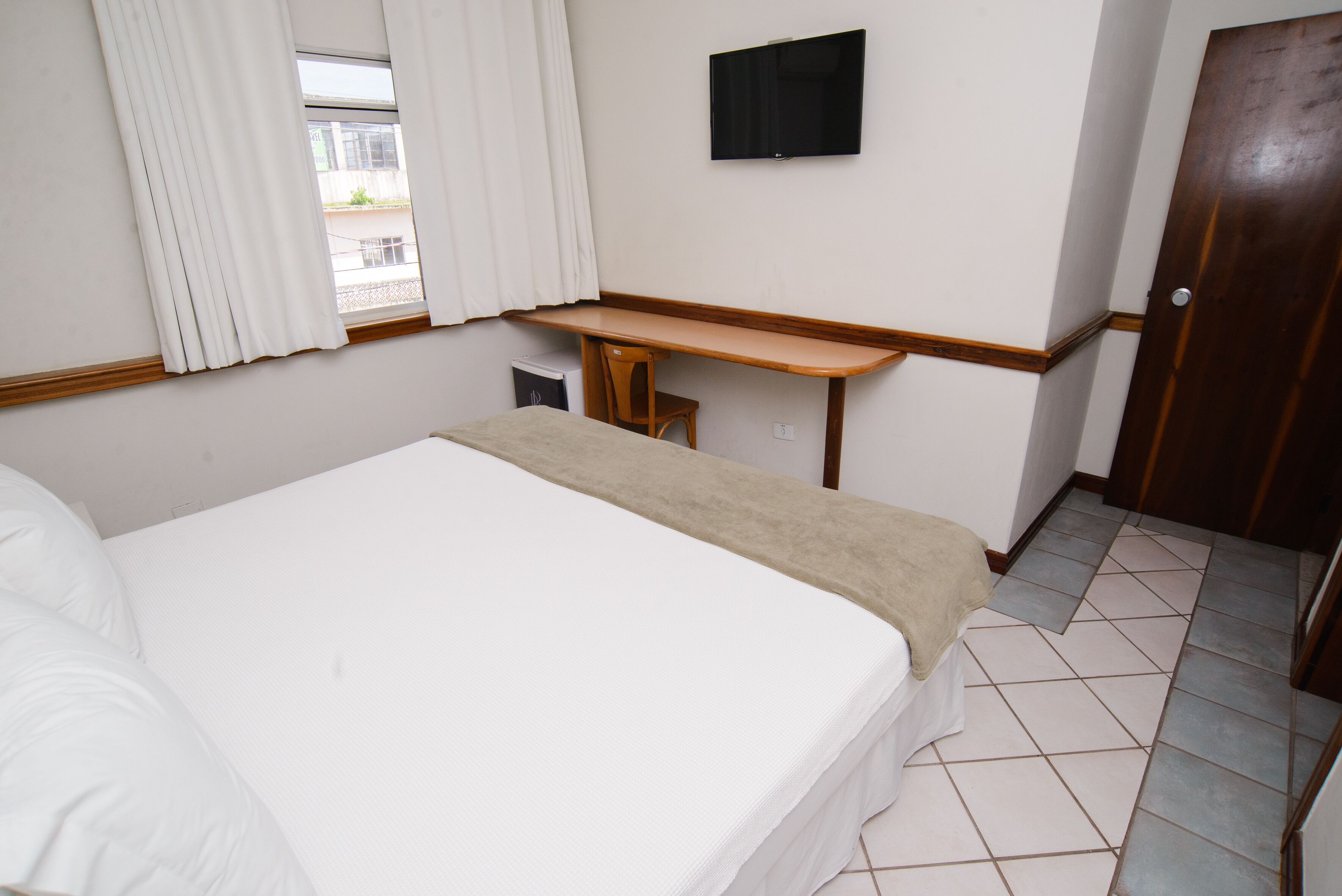 Een hotelkamer met een bed, bureau, televisie en een deur.