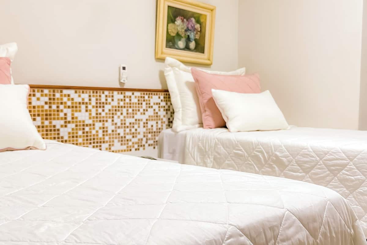 Two beds with white bedding, a mosaic-patterned headboard, and a framed floral painting on the wall.