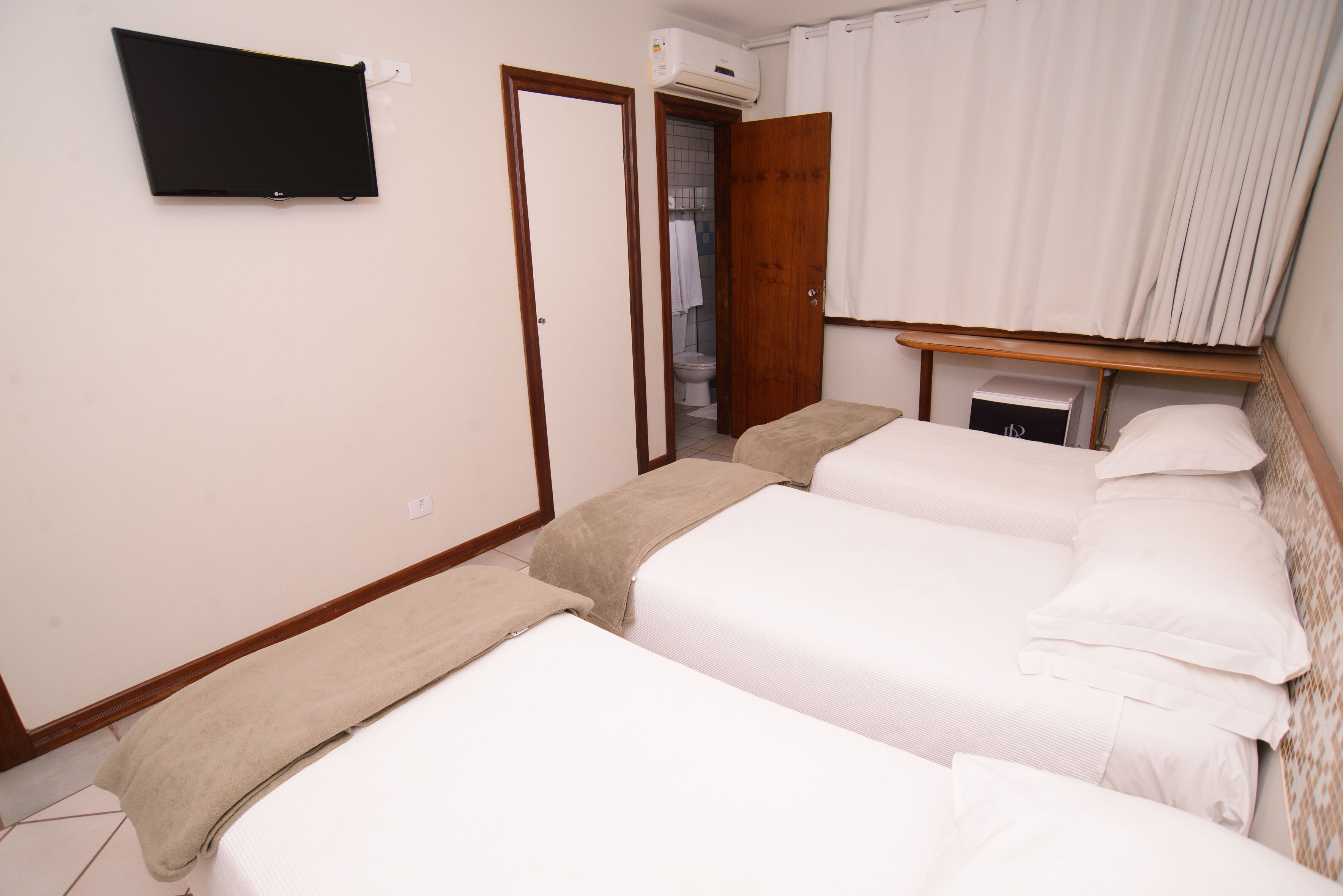Ein Hotelzimmer mit zwei Betten, einem hölzernen Kopfteil, einem Flachbildfernseher und einer Klimaanlage.