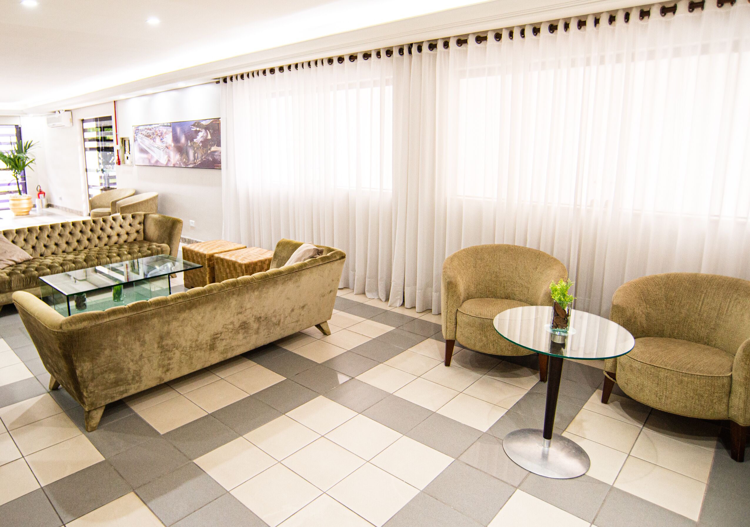 A living room with a sofa, armchairs, a glass coffee table, and a large window with curtains.