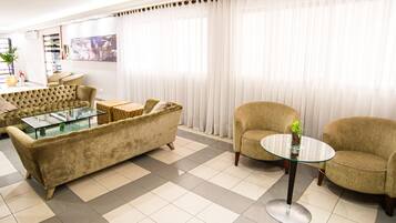 A living room with a sofa, armchairs, a glass coffee table, and a large window with curtains.