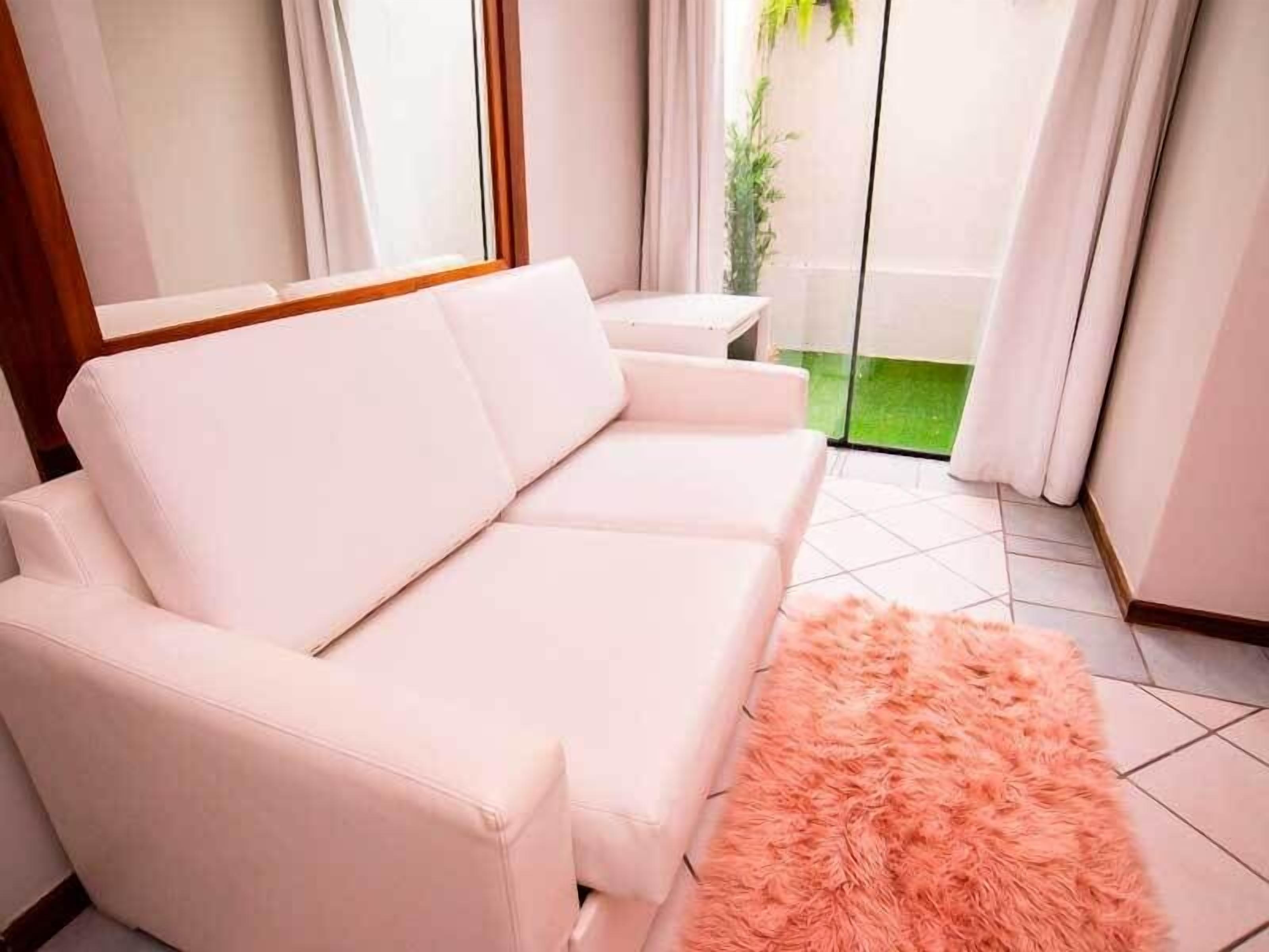 Ein weißes Sofa in einem Raum mit Fliesenboden und einem flauschigen pinkfarbenen Teppich.
