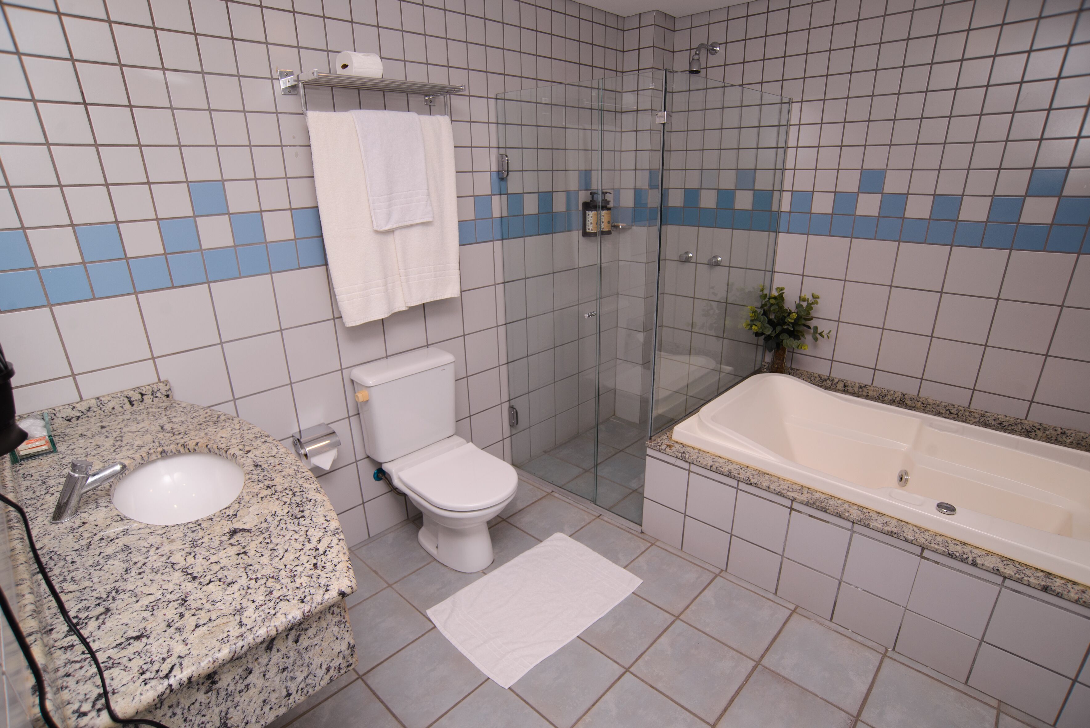 Un baño con lavamanos de encimera de granito, inodoro, ducha con mampara de vidrio y bañera.