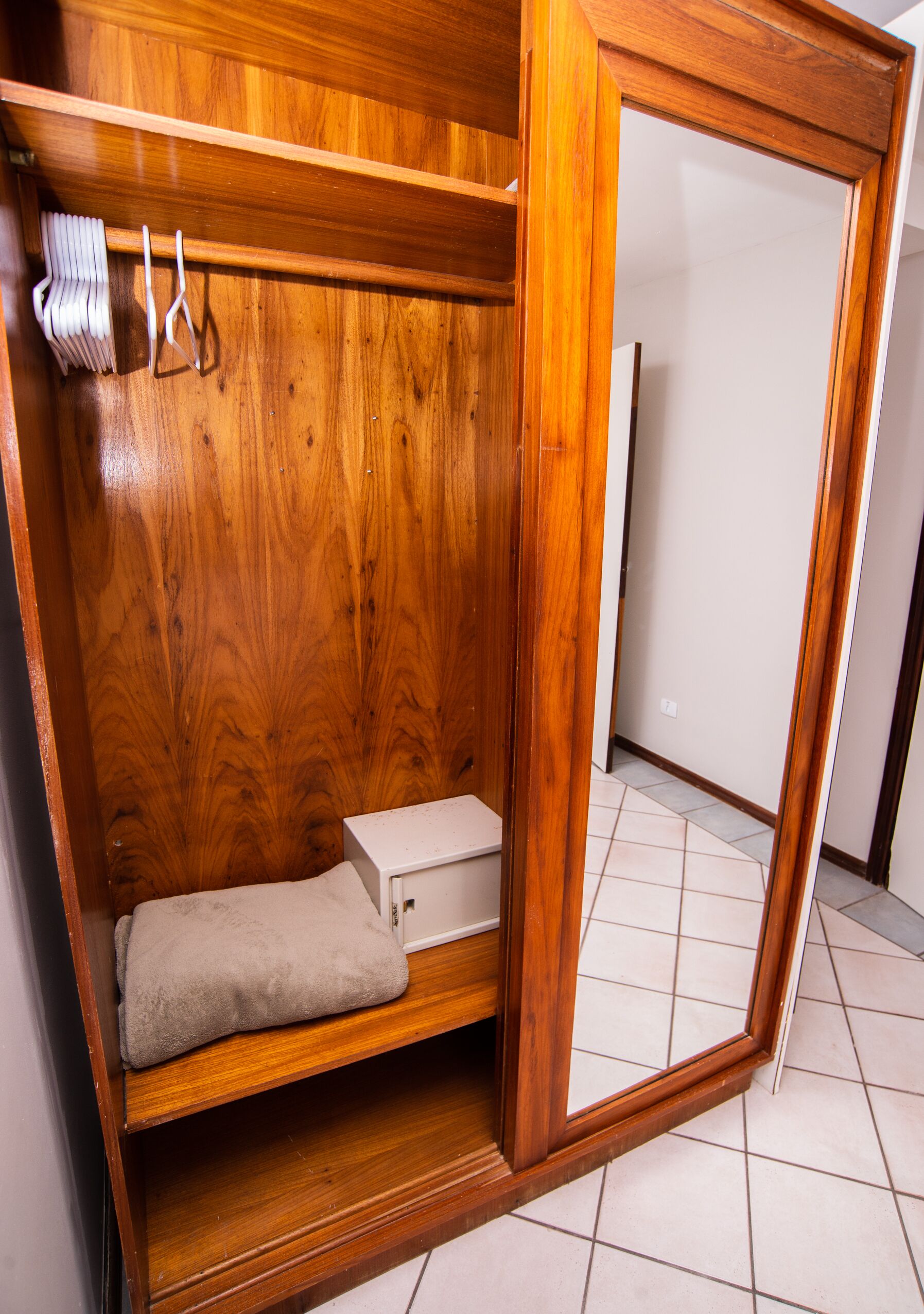 A wooden wardrobe with a mirror, a hanging rack, and a small shelf.