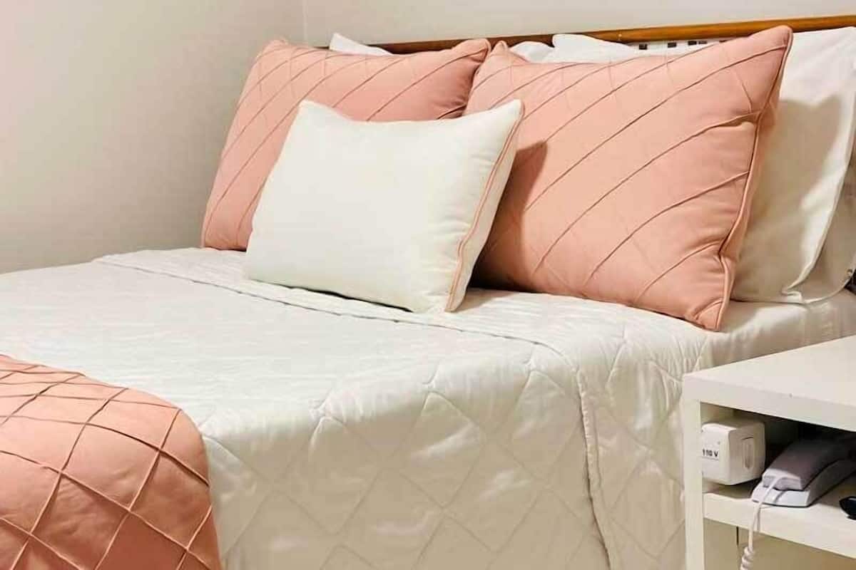 A neatly made bed with a quilted white and peach bedding, a white pillow, and peach pillows with a diamond pattern.