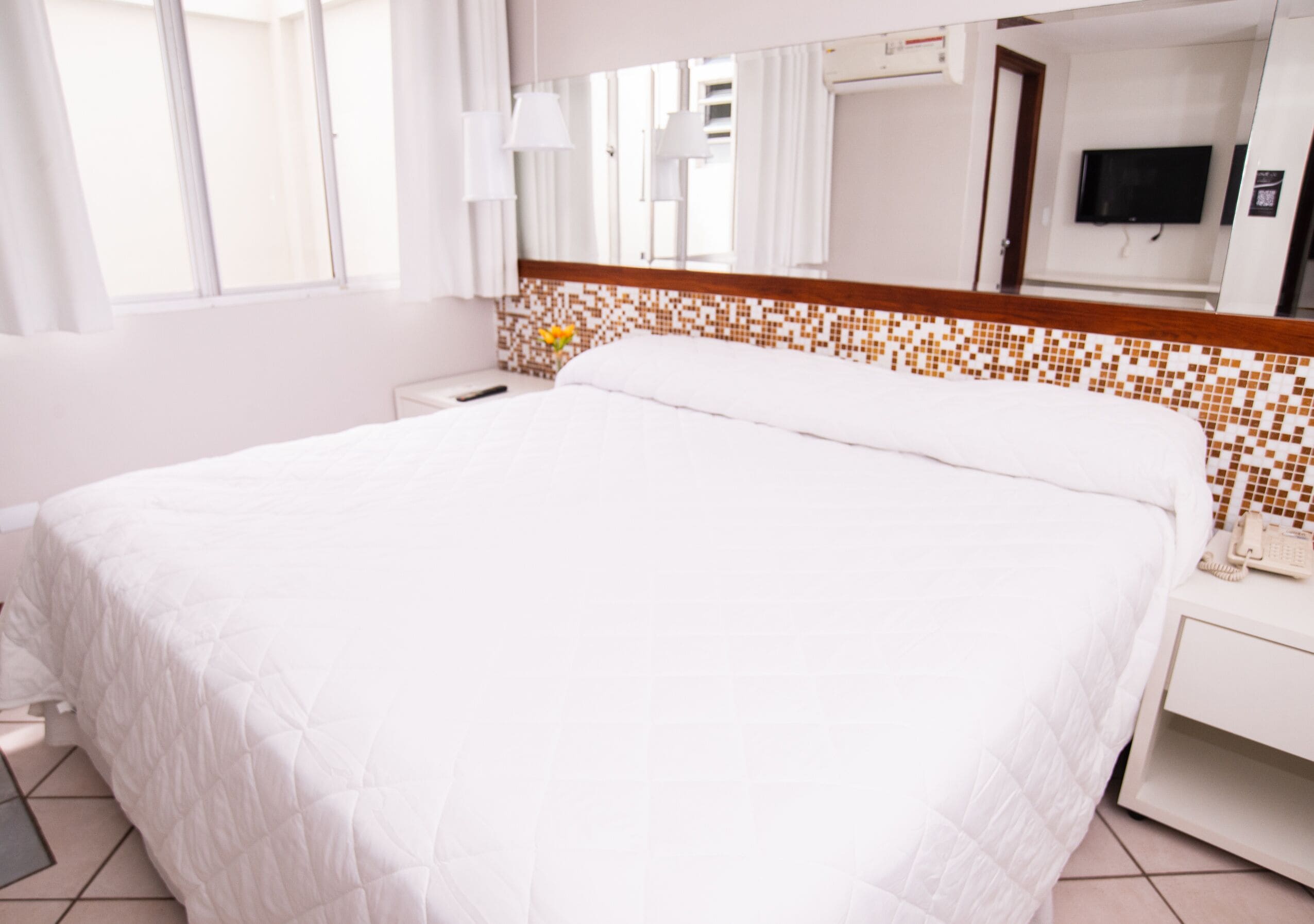 Habitación de hotel con una cama grande, una mesita de noche con un teléfono, una pequeña mesa con un florero y un televisor en la pared.