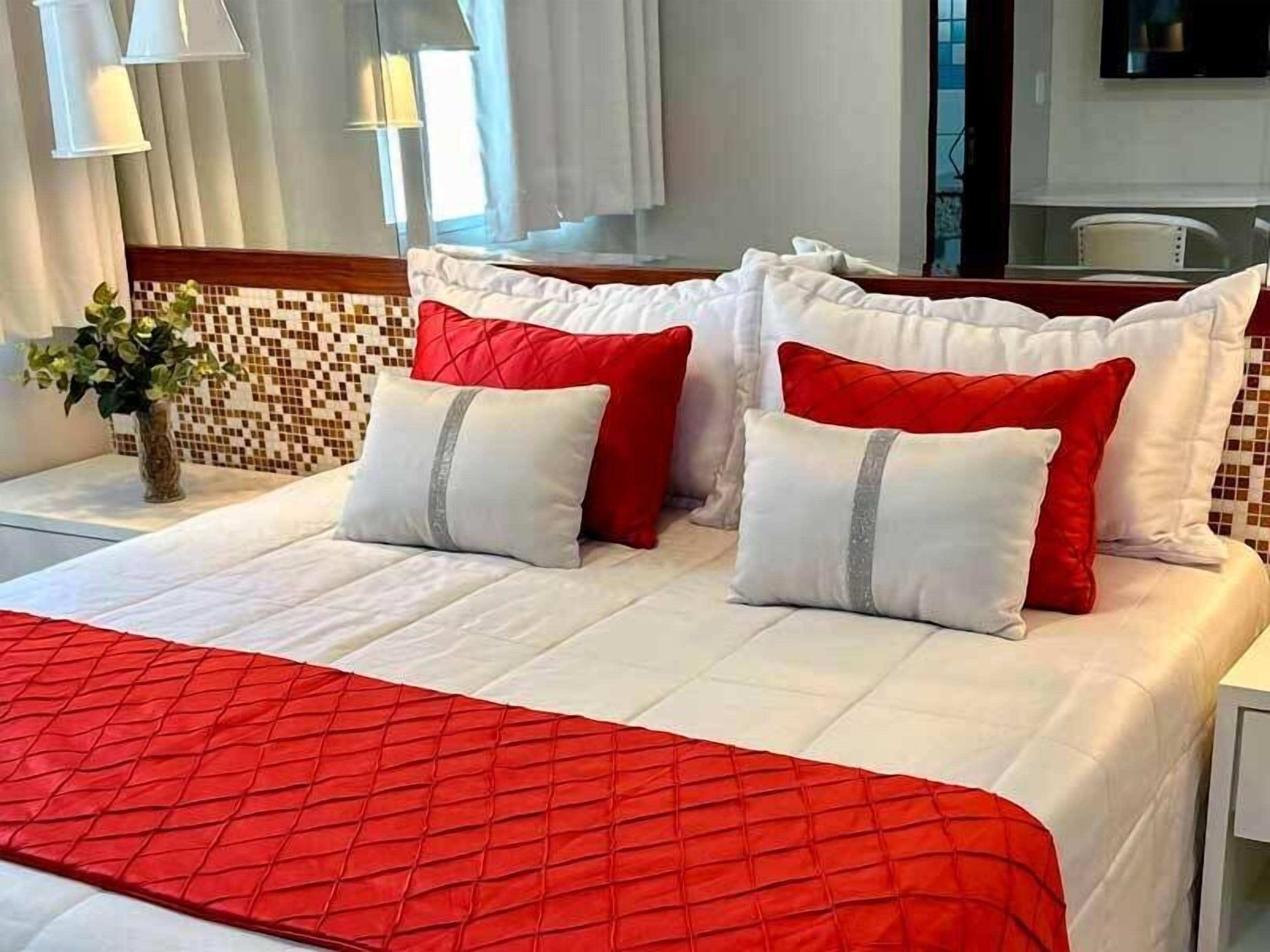 A hotel room with a neatly made bed, a vase with flowers, and a tiled wall.