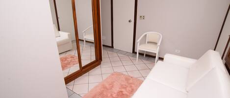 A room with a white sofa, a white chair, a pink rug, and a large mirror.