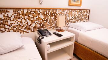 A hotel room with two beds, a bedside table with a phone and remote, a wall-mounted thermostat, and a framed picture on the wall.