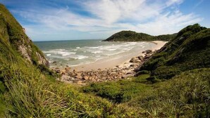 Paisaje costero con playa, costa rocosa y vegetación exuberante.
