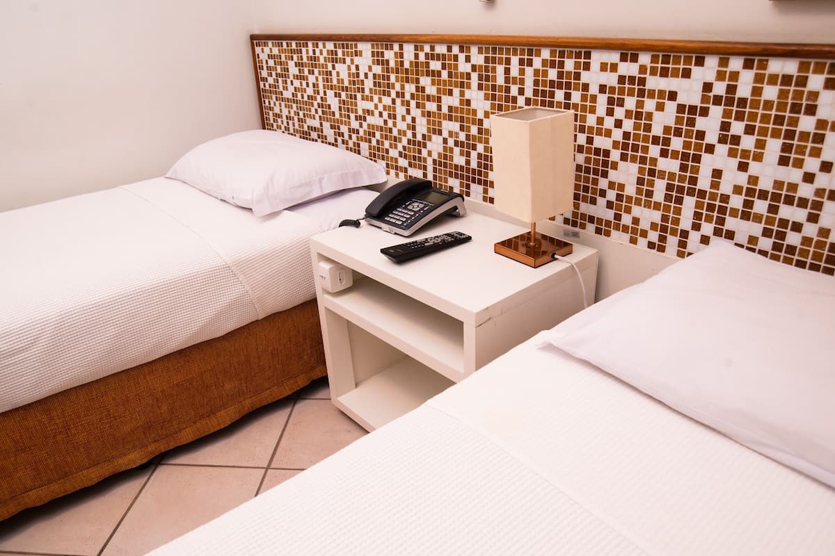 A hotel room with two beds, a bedside phone, a lamp, and a tiled wall.
