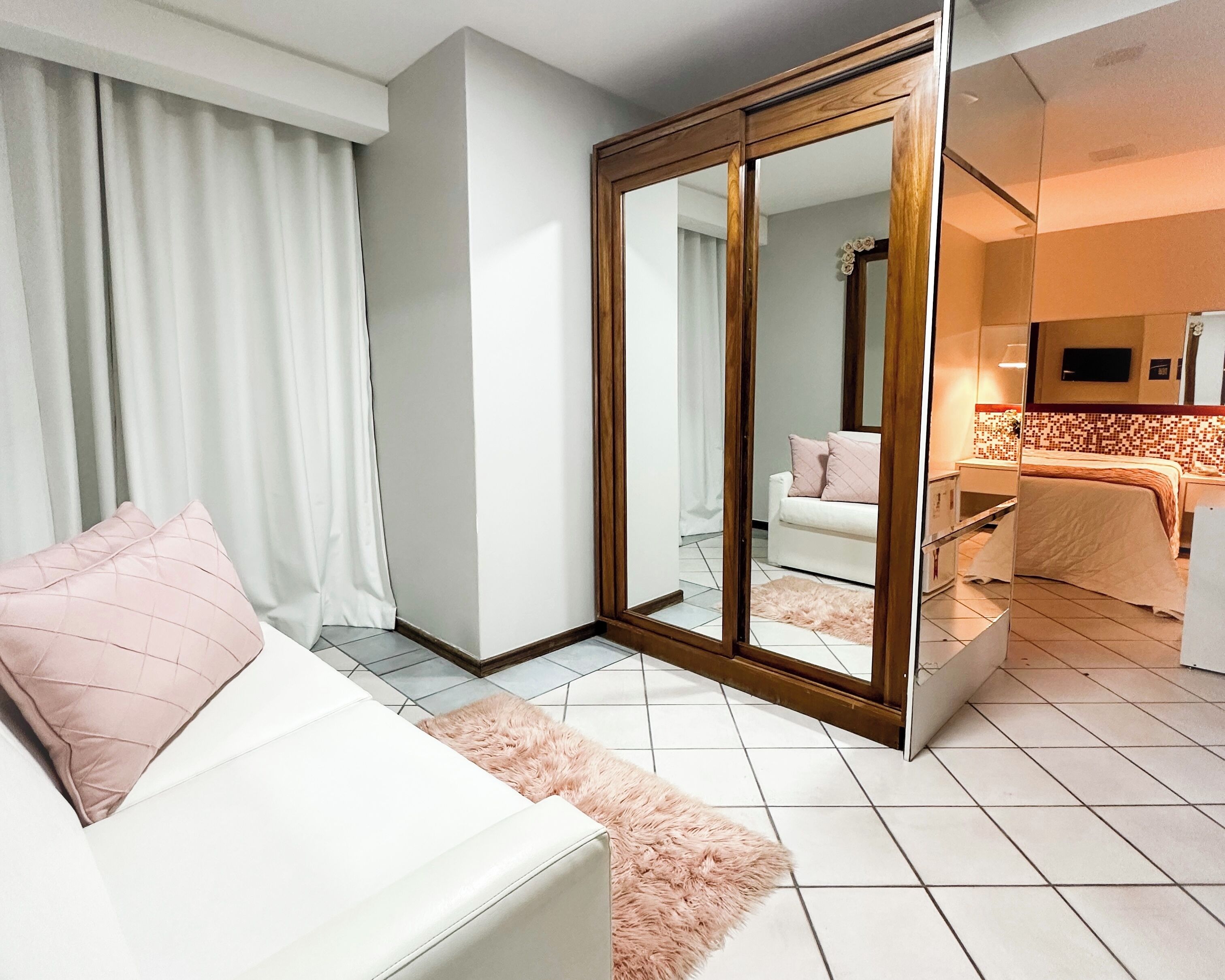 A modern hotel room with a large mirror, a white sofa, a fluffy rug, and a neatly made bed.