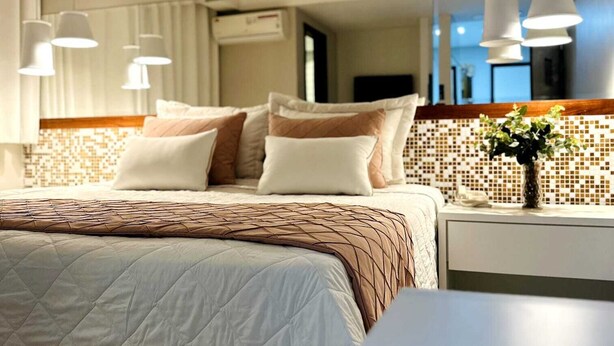 Una habitación de hotel moderna con una cama grande, una mesita de noche con un florero y un espejo sobre la cama.