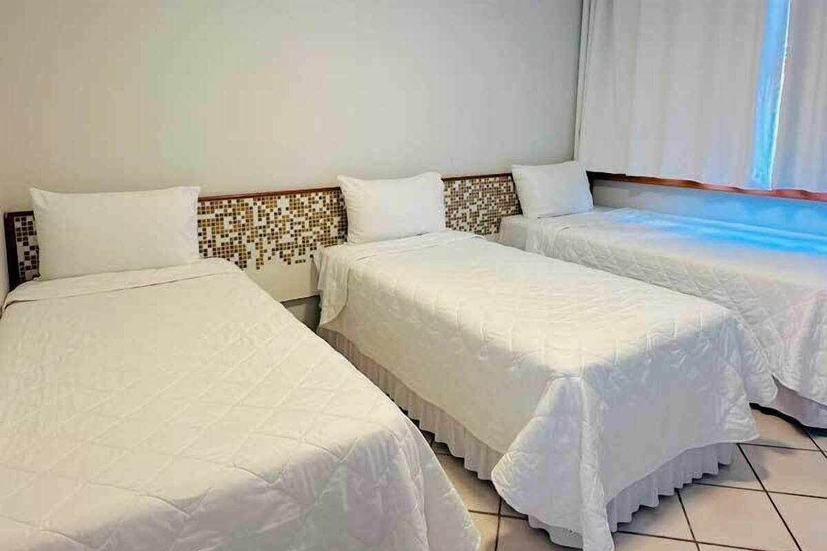 A hotel room with two beds, white bedding, a tiled floor, and a patterned headboard.