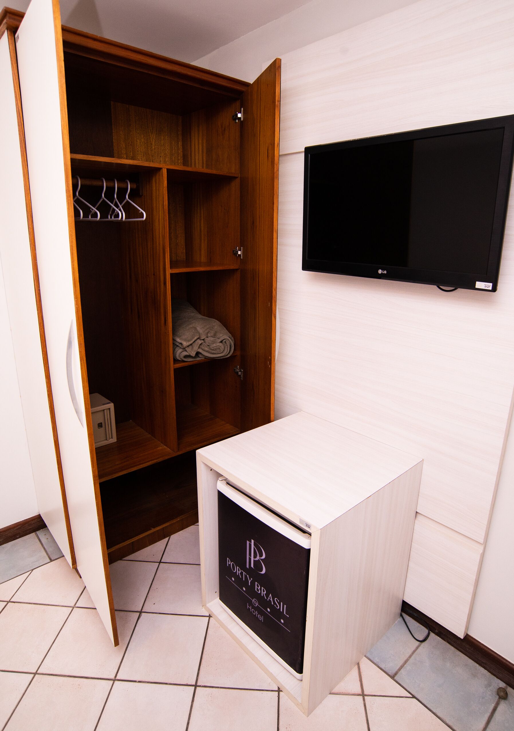 Una habitación con un armario de madera, un televisor de pantalla plana montado en la pared y un pequeño mueble blanco con un logotipo.