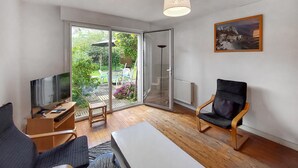 Una sala de estar moderna con televisor, sofá, sillón y un gran ventanal corredera que da a un jardín.