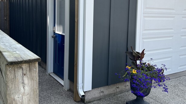 Rakennuksessa on autotalliovi, puinen penkki ja kukilla koristeltu kukkaruukku.